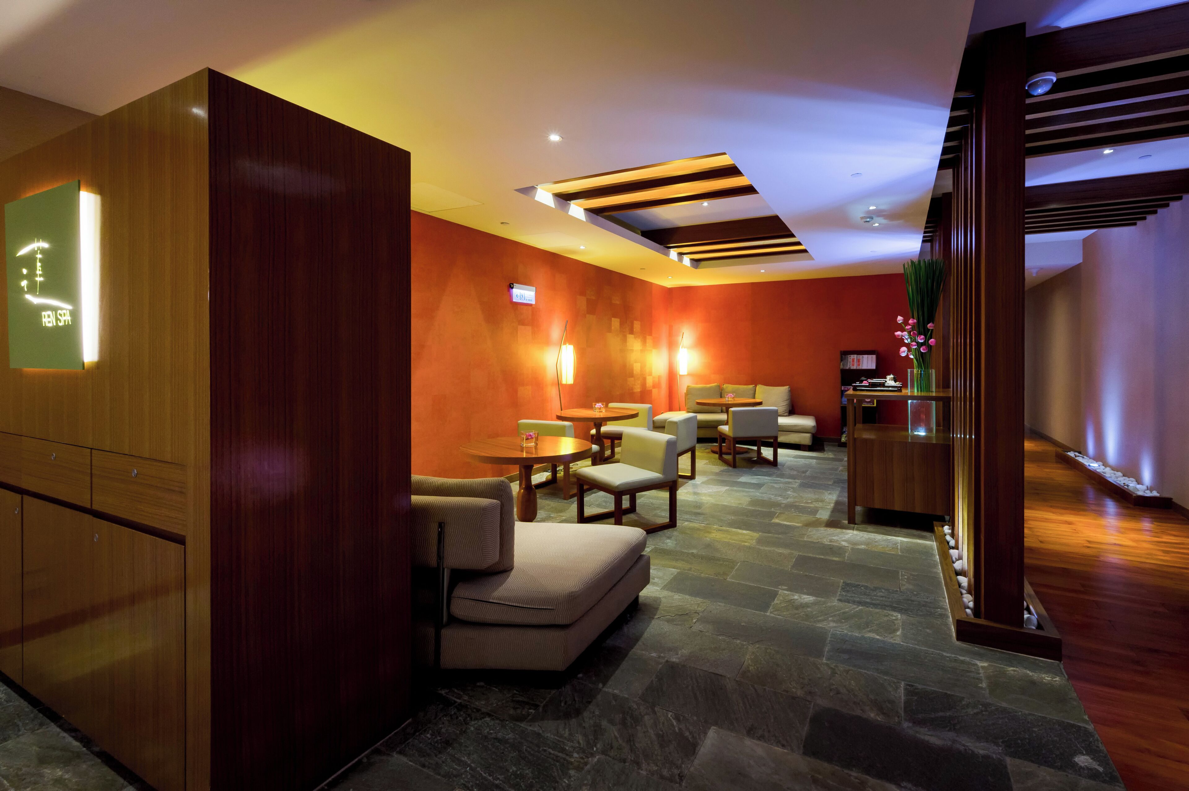 Een moderne hotellobby met houten lambrisering, stenen vloer en een zithoek met ronde tafels en stoelen.