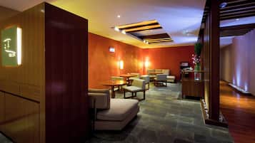Een moderne hotellobby met houten lambrisering, stenen vloer en een zithoek met ronde tafels en stoelen.