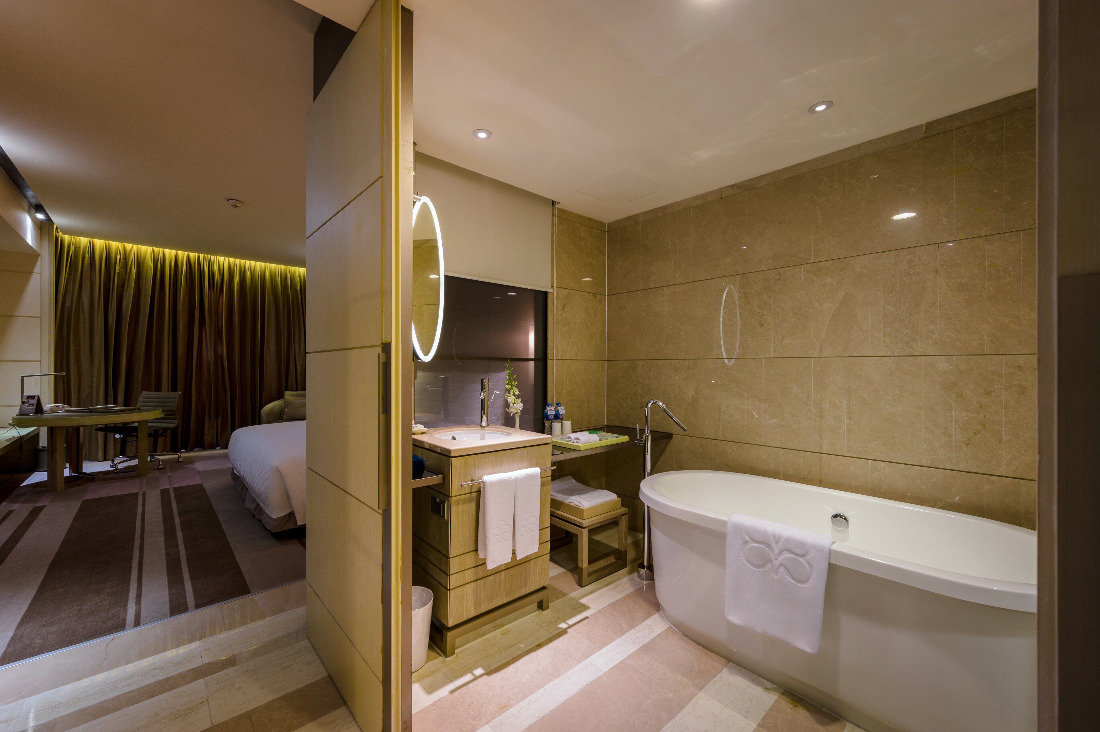 A modern hotel bathroom with a large bathtub, a vanity with a mirror, a sink, and a shower area.