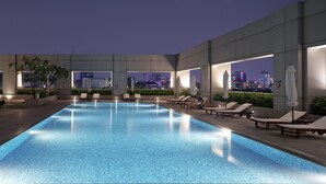 Una piscina en la azotea con sillones y sombrillas, con vistas a un horizonte urbano nocturno.