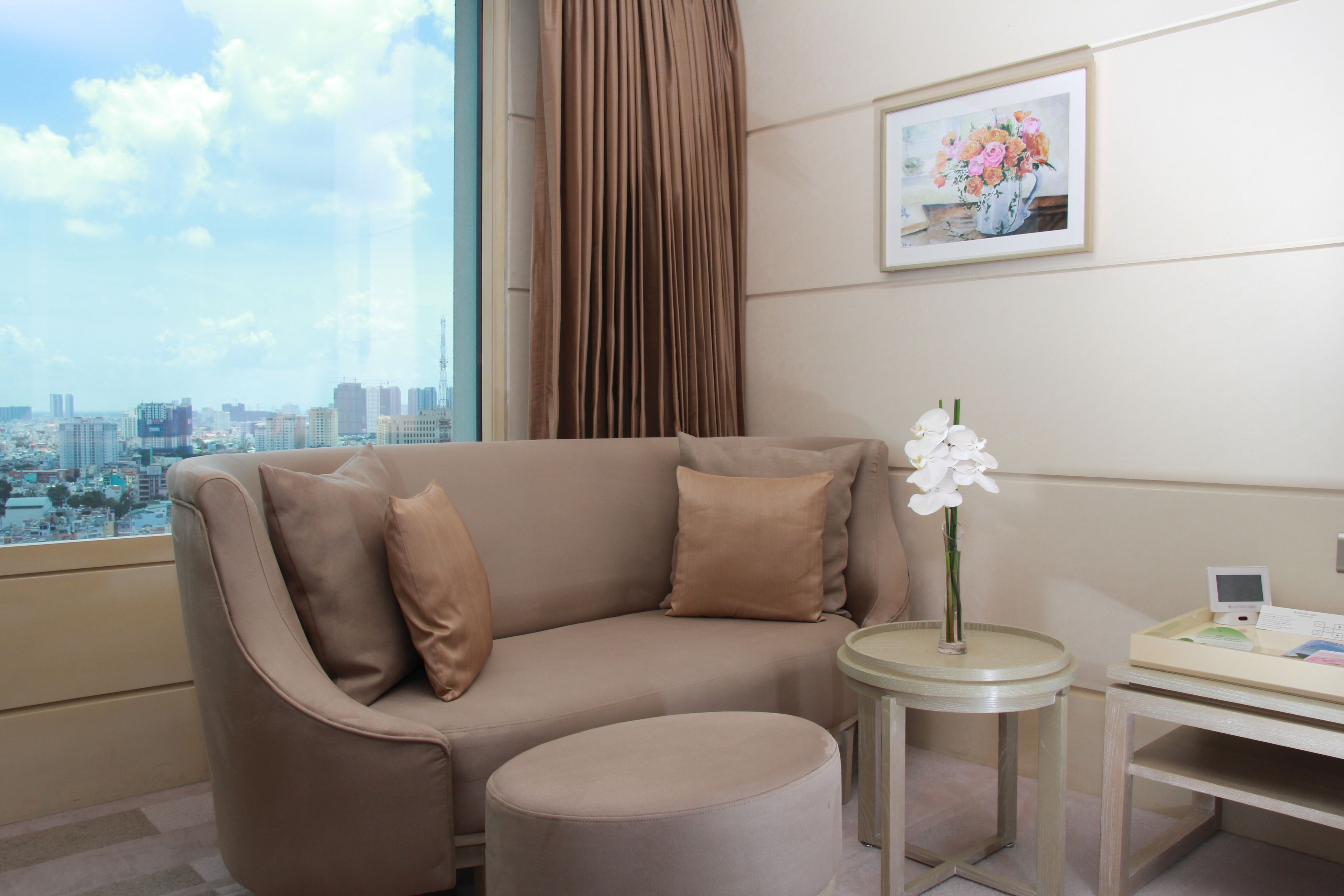 A modern hotel room with a sofa, ottoman, and a small table with a vase of flowers.