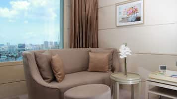 A modern hotel room with a sofa, ottoman, and a small table with a vase of flowers.