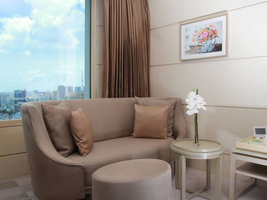 A modern hotel room with a sofa, ottoman, and a small table with a vase of flowers.