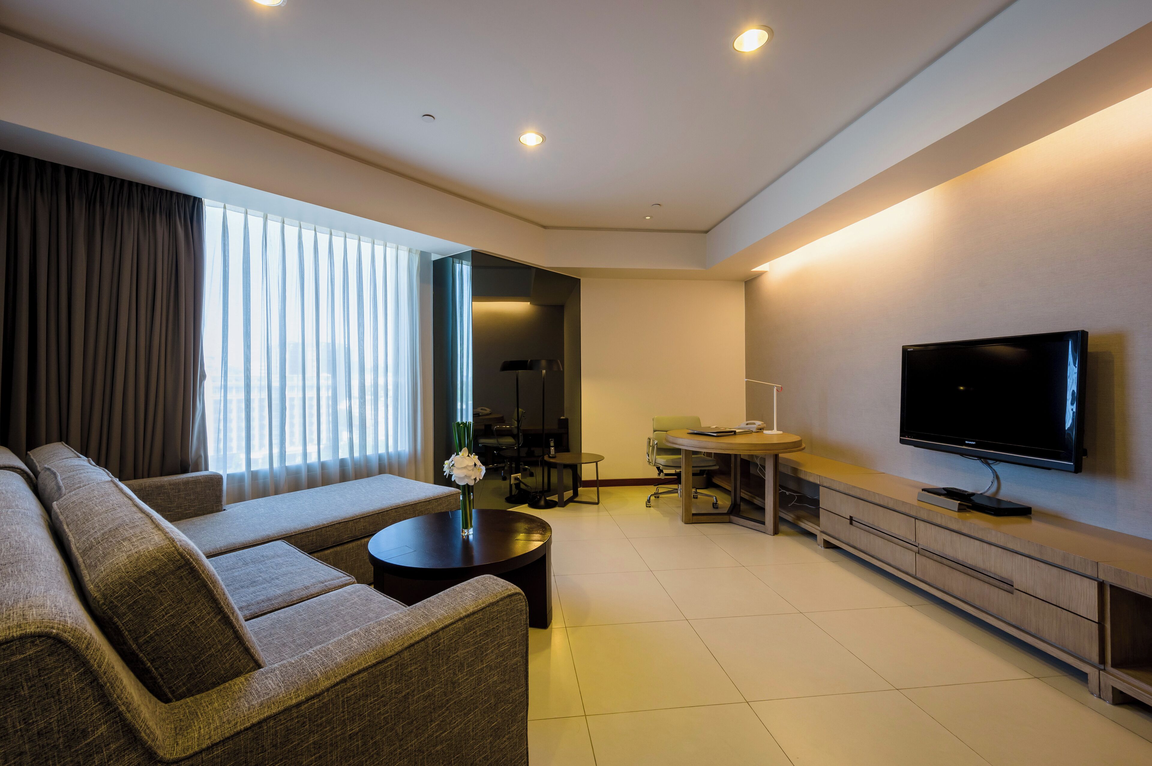 A modern living room with a sofa, a coffee table, a flat-screen TV, and a dining area with a table and chairs.