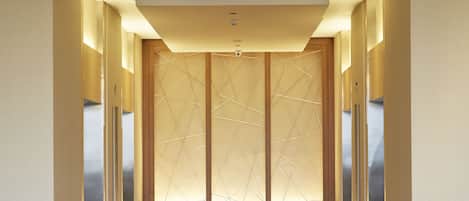 A modern hotel corridor with a central wooden partition, a large circular light fixture, and a clean, polished floor.