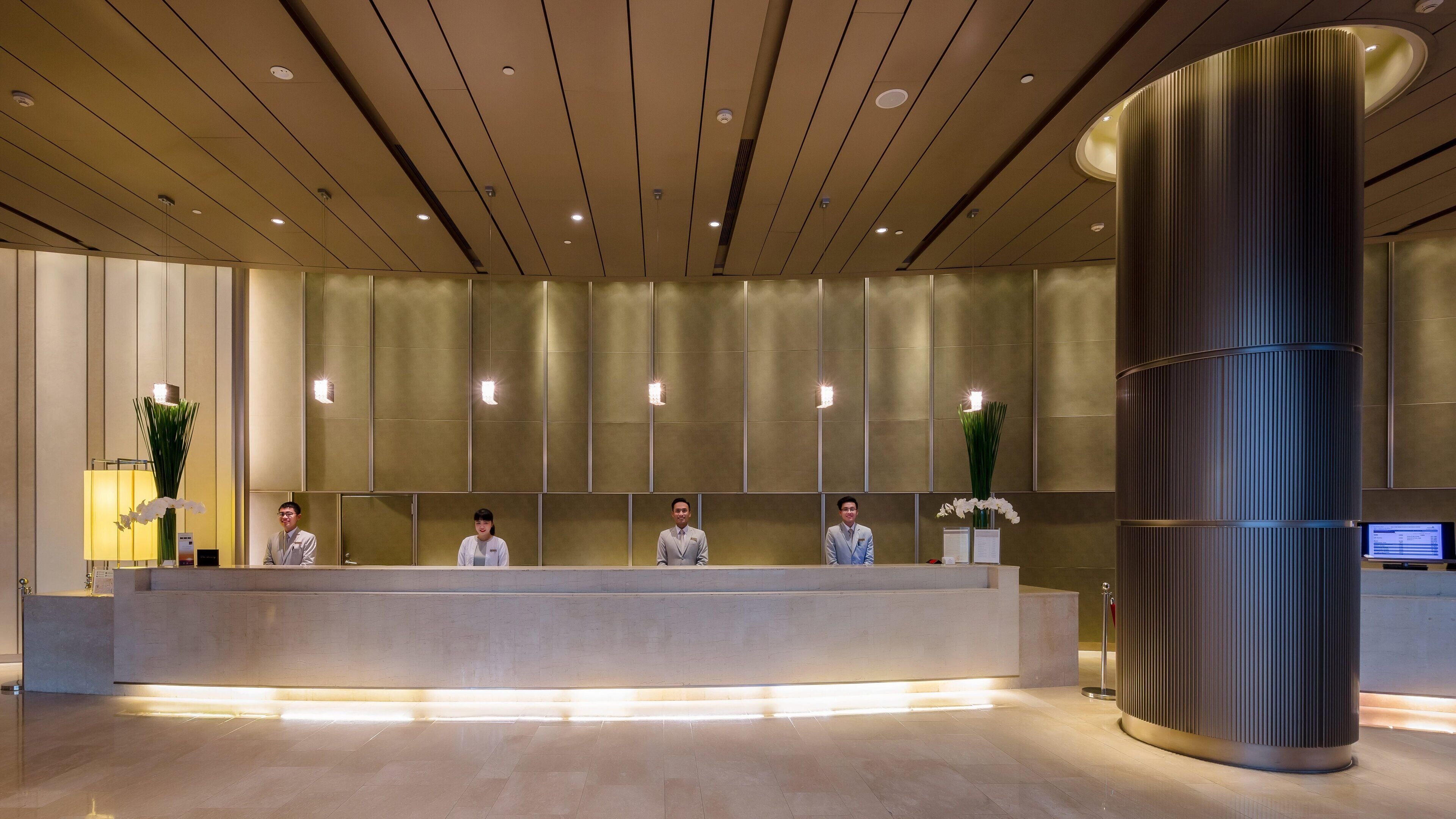 A reception area with a modern design, featuring a reception desk, a large cylindrical column, and a wall-mounted information screen.