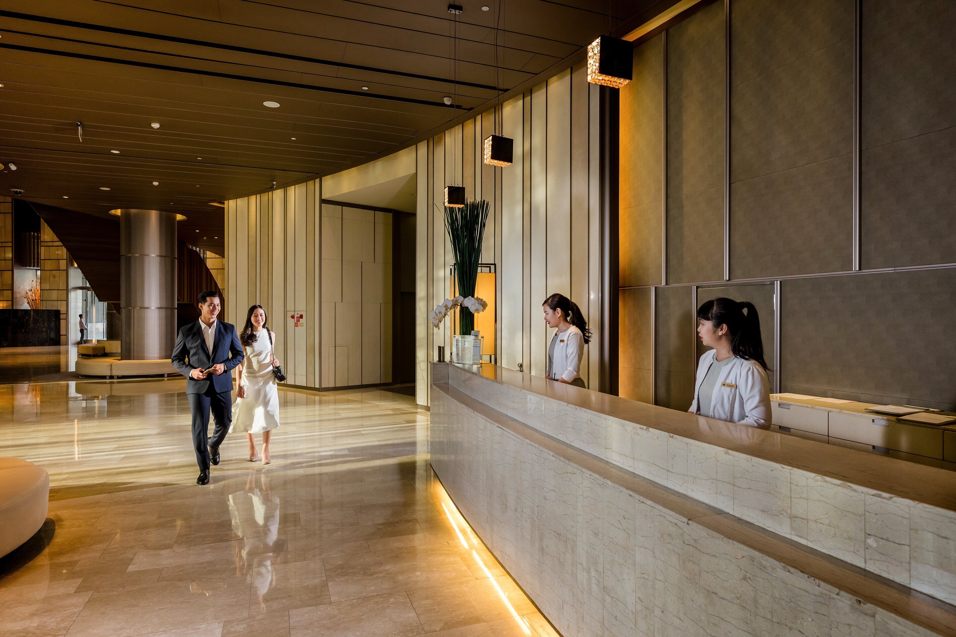 A hotel reception area with a modern design, featuring a reception desk, a large plant, and a polished marble floor.