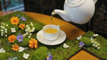 A white teapot pouring tea into a cup on a saucer, surrounded by a decorative table with moss and flowers.