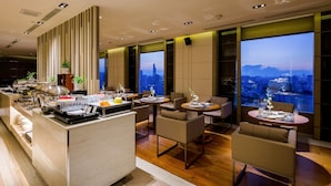 A modern hotel lobby with a buffet area, seating arrangements, and large windows offering city views. - Hotel Nikko Saigon (Ho Chi Minh City)