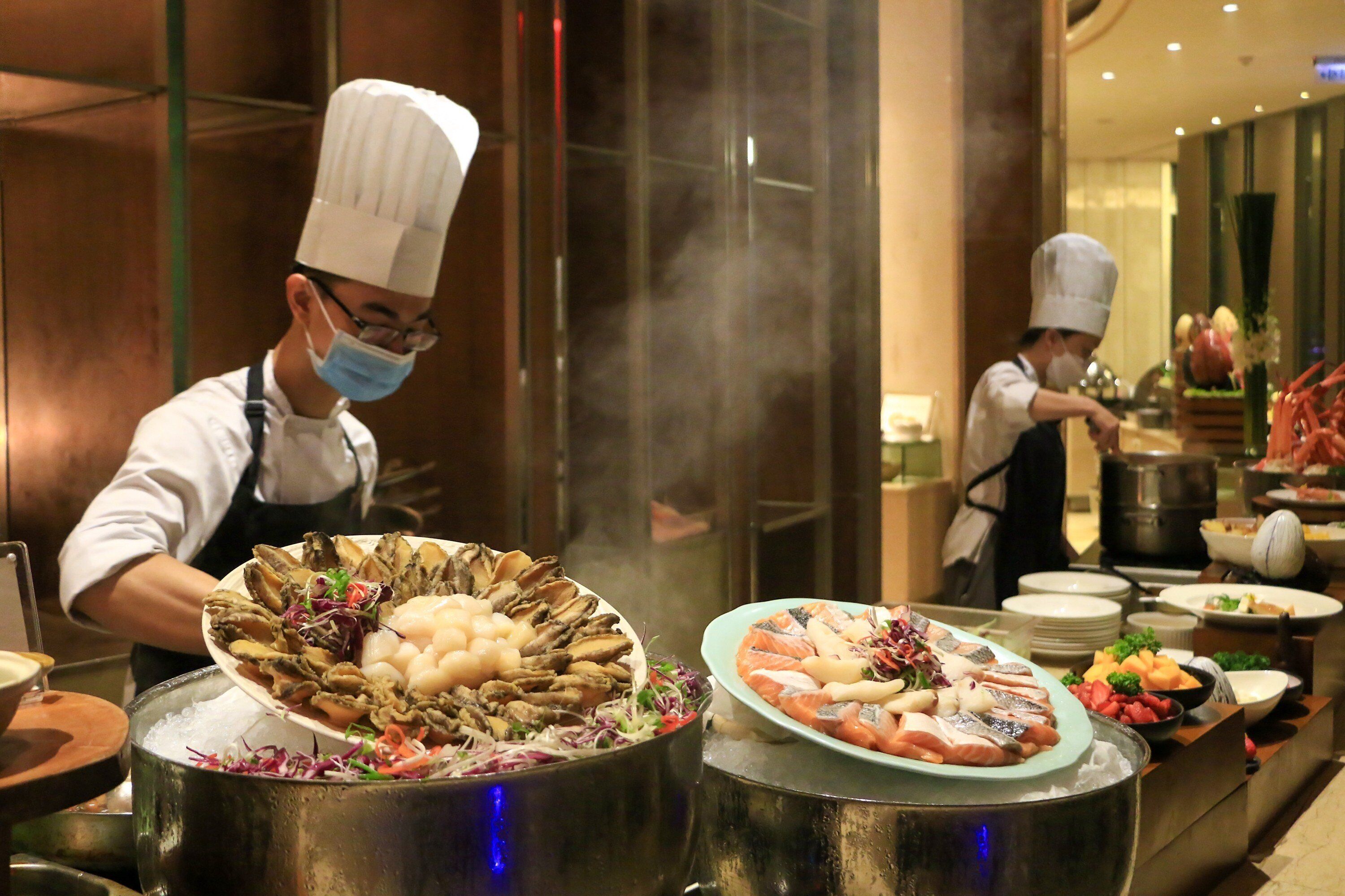 Chefs preparing seafood dishes in a professional kitchen with stainless steel equipment and a modern design.