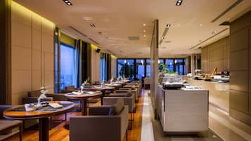 A modern hotel lobby with a long reception desk, multiple seating areas, and large windows offering city views.