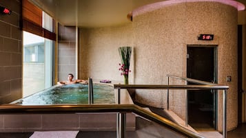 A hot tub with a person relaxing, a temperature display, and a wall with a textured pattern.