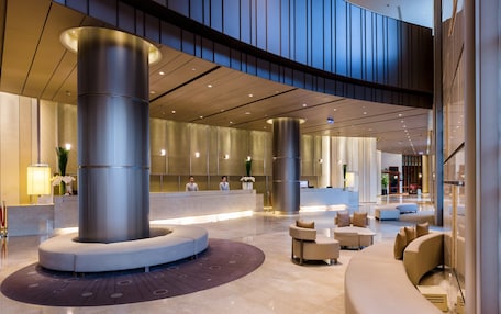 A modern lobby with a reception desk, seating areas, and a large central column.
