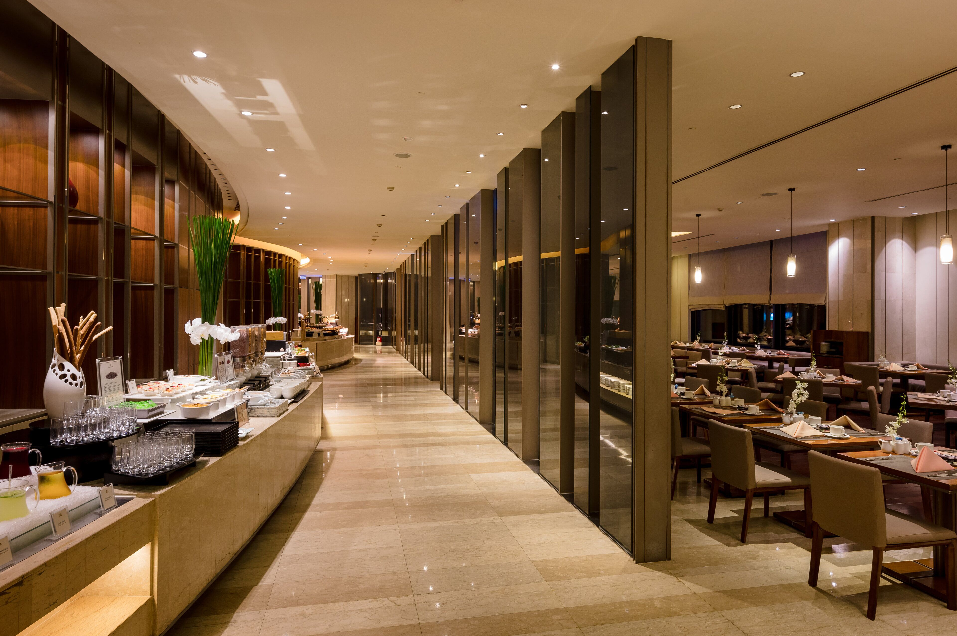 Un hall d’hôtel comprenant un long comptoir d’accueil, un espace buffet et une salle à manger avec des tables et des chaises.