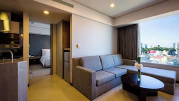 A modern hotel room with a sofa, a coffee table, a view of the city, and a kitchenette.