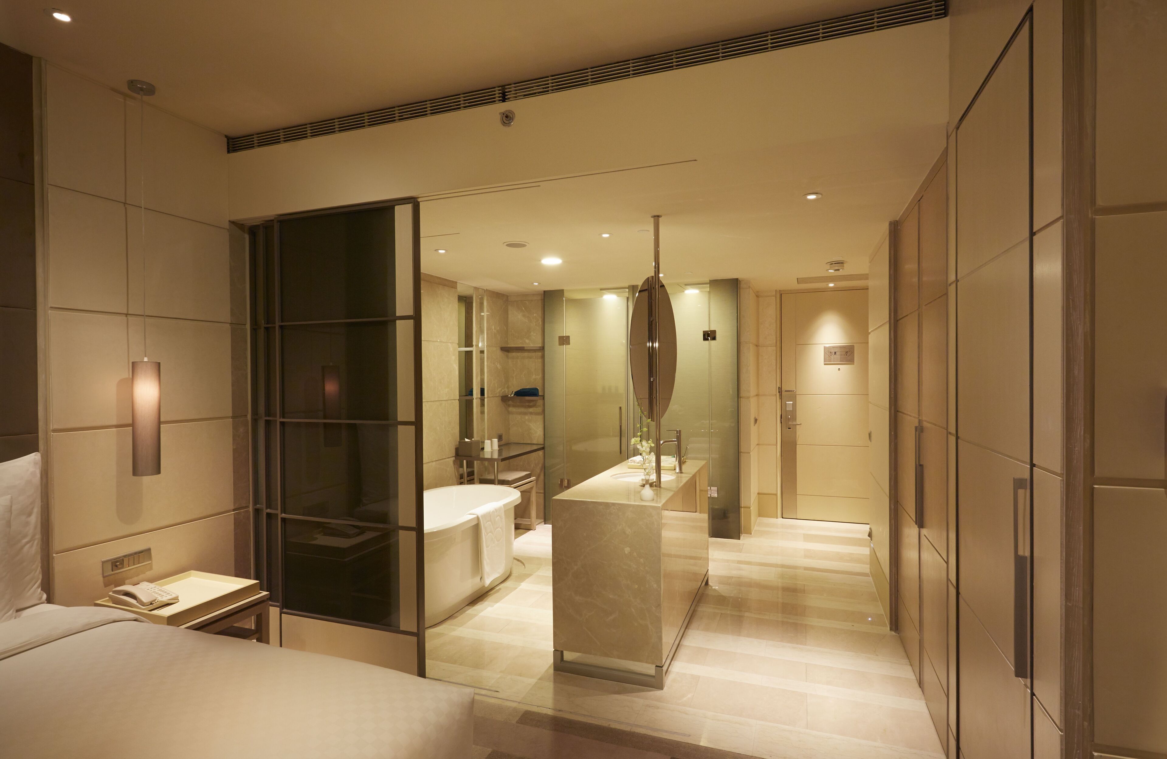 A modern hotel room with a large bed, a separate bathroom, a vanity with a mirror, and a walk-in closet.