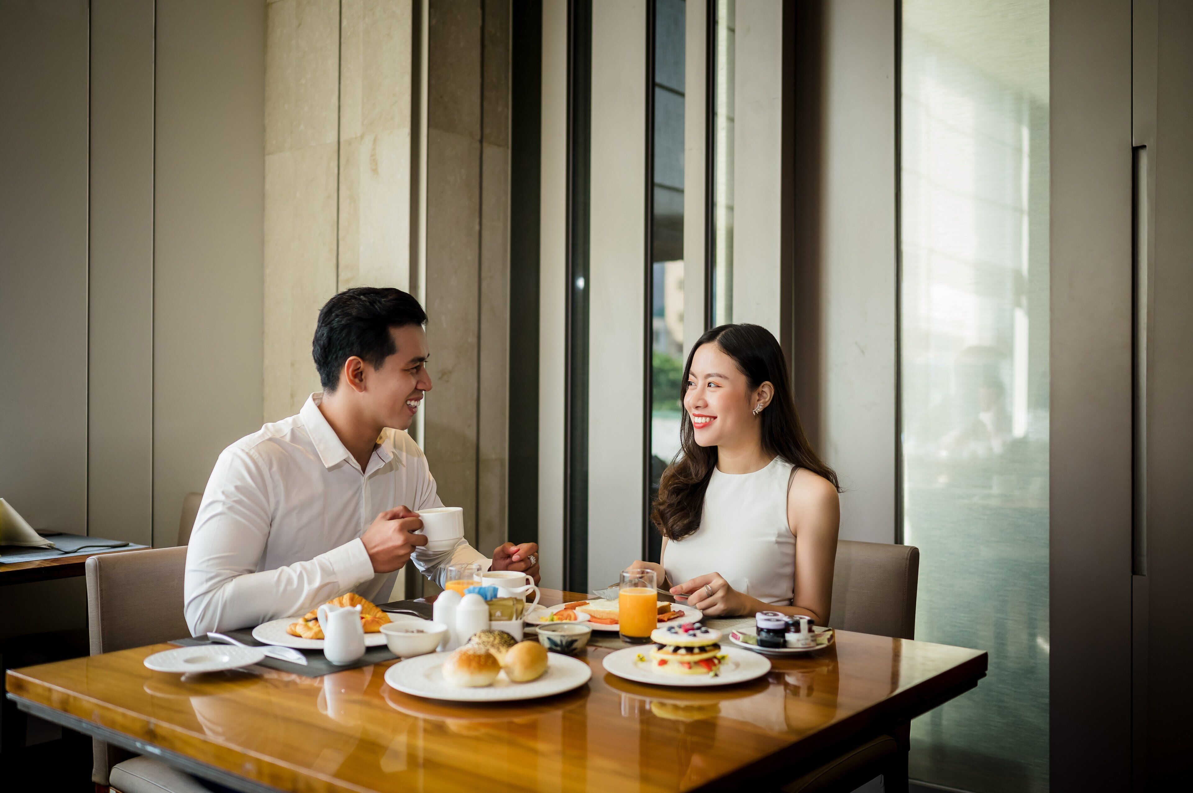 A breakfast setting with a table set for two, featuring plates with eggs, pastries, and juice.