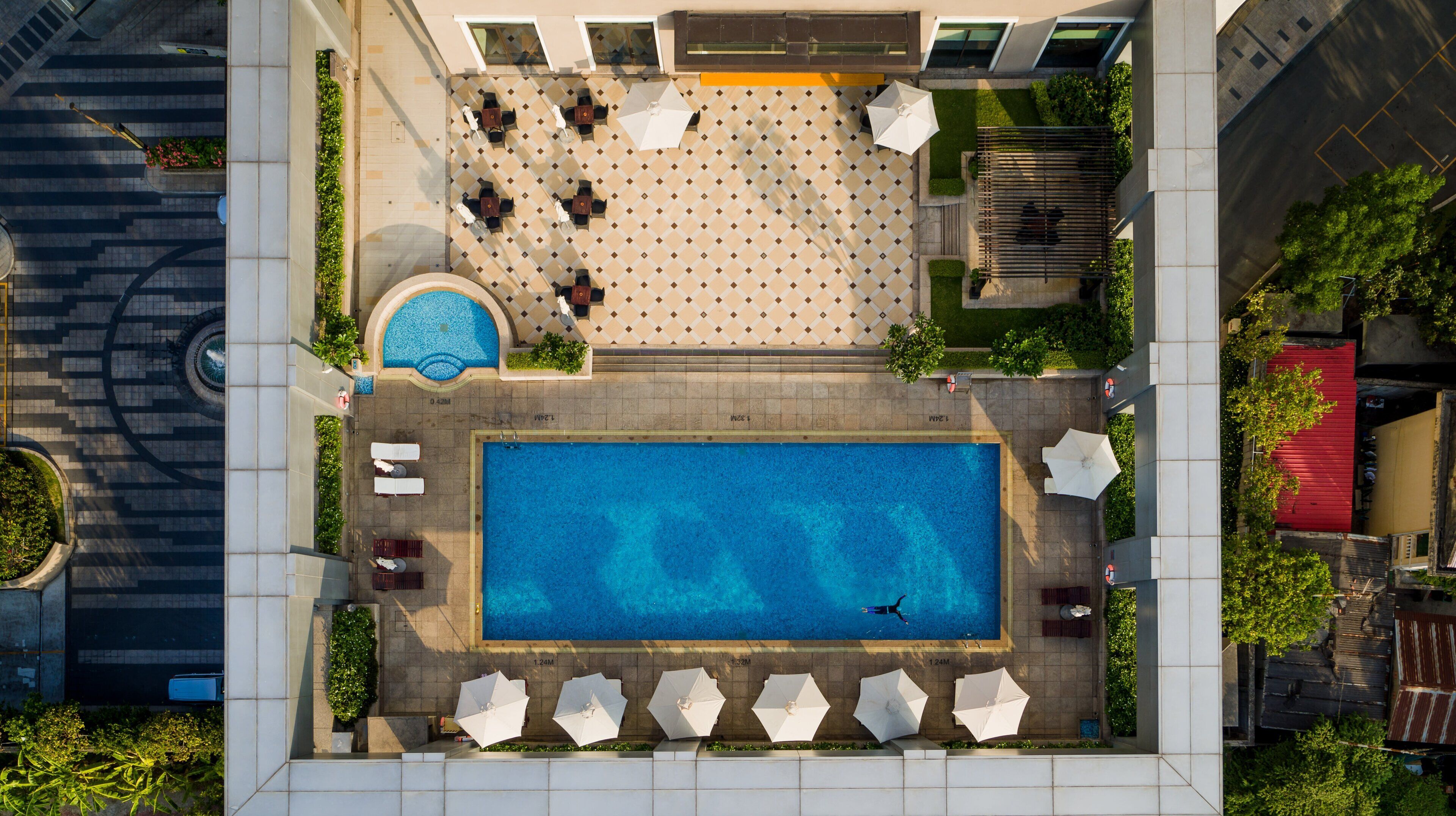 Vista aérea de un área de piscina en la azotea, con piscina rectangular, sillas de descanso y sombrillas.