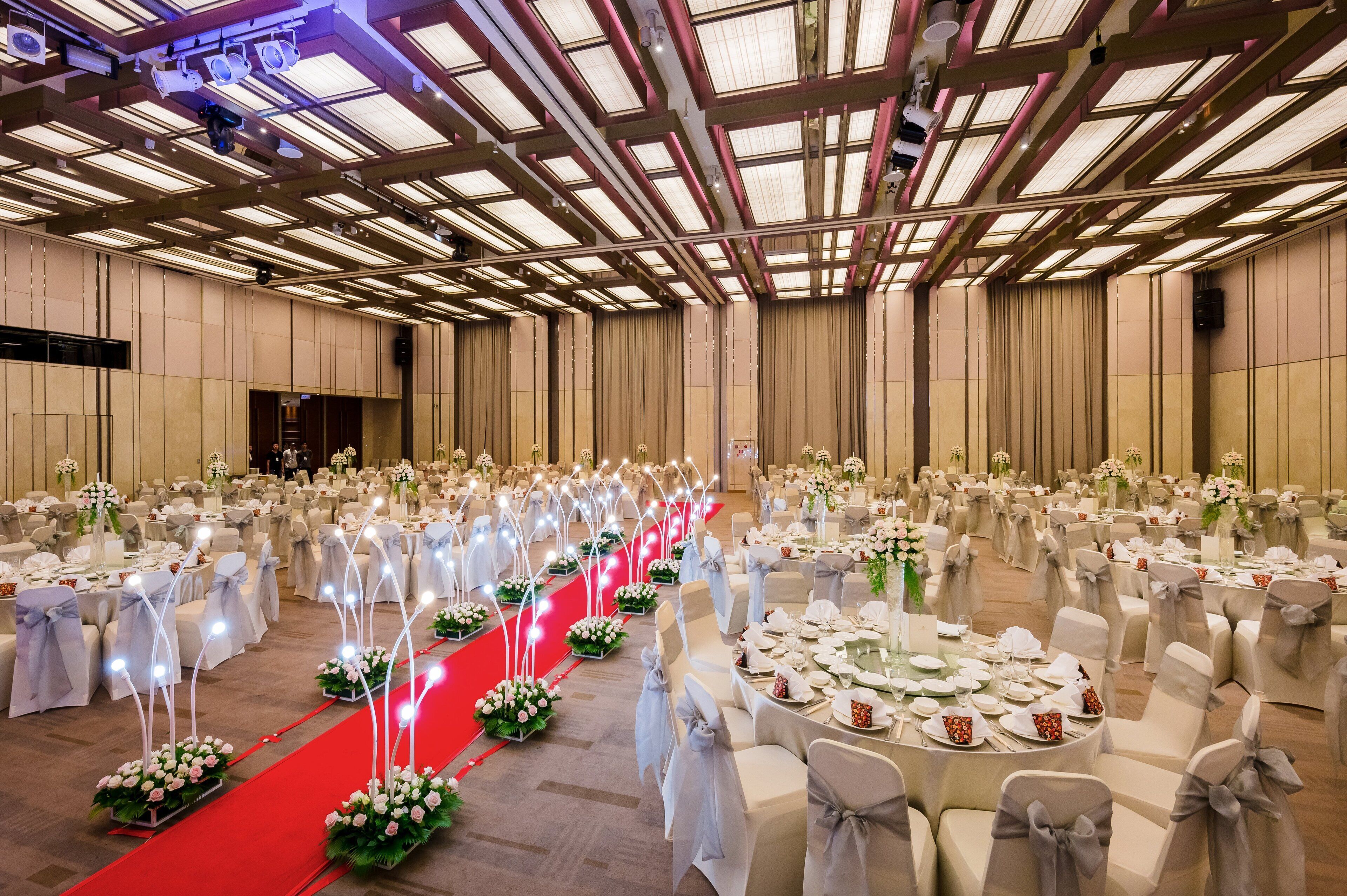 Ein großer Festsaal mit gedeckten Tischen für eine festliche Veranstaltung, mit rotem Teppich und floralen Tischdekorationen.