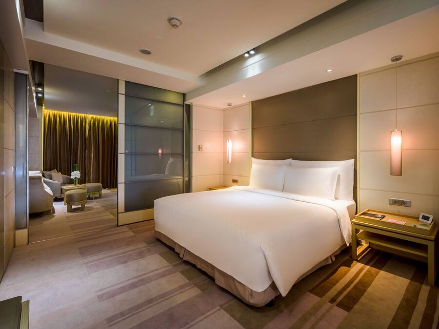 A modern hotel room with a large bed, bedside tables, a sofa, and a view of the cityscape.