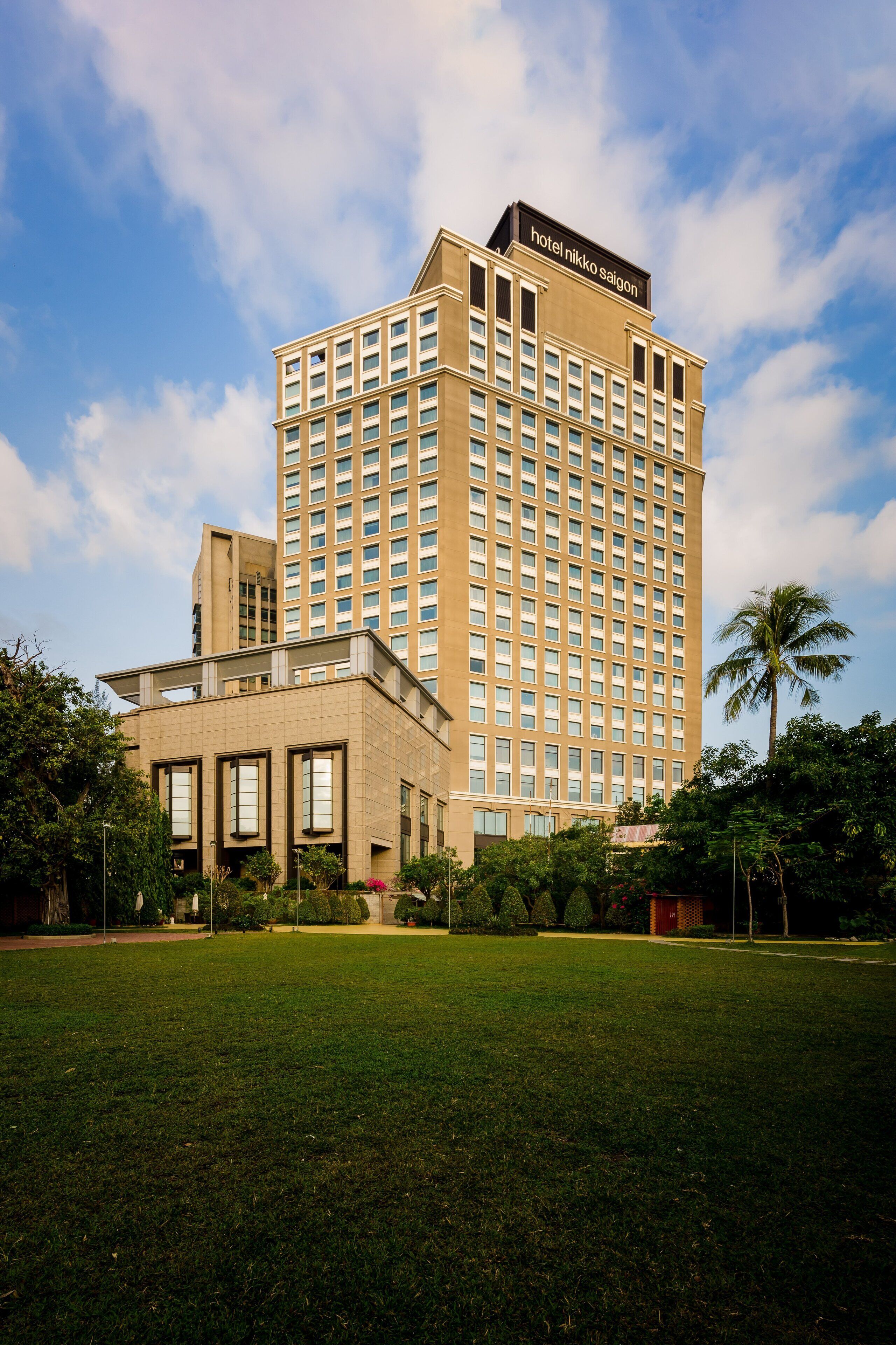A tall hotel building with a sign reading "hotel nikko saigon" and a well-maintained lawn in front.