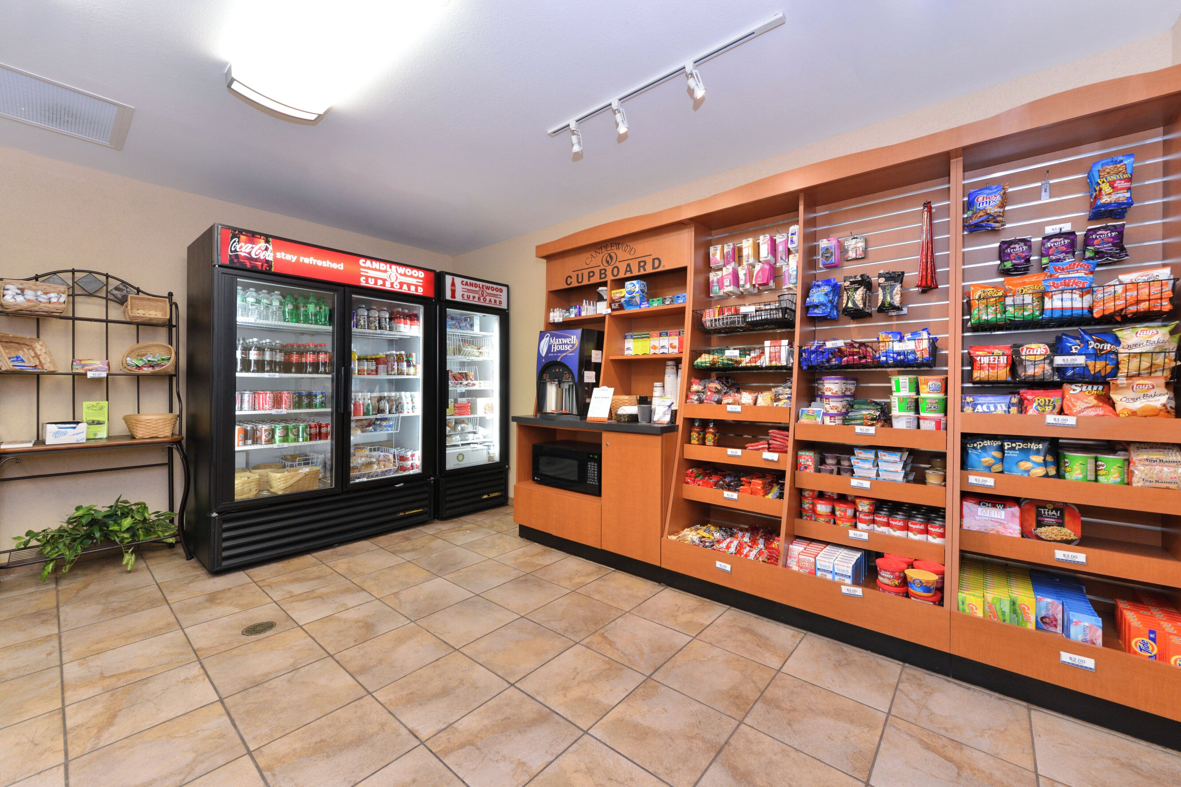A grocery store interior with refrigerated beverage dispensers, a self-serve coffee station, and shelves stocked with snacks and household items.