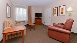 Habitación de hotel con sofá, una mesa de madera, televisión, lámpara y cuadros en la pared.