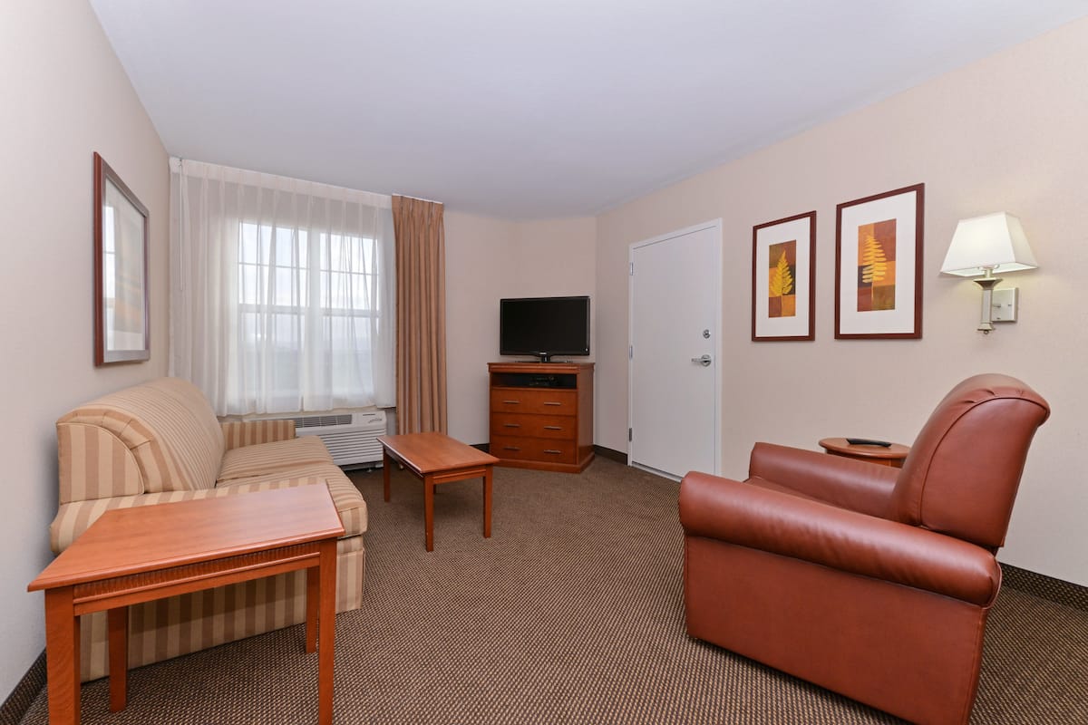 Ein Hotelzimmer mit einer Couch, einem Holztisch, einem Fernseher, einer Lampe und gerahmten Bildern an der Wand.