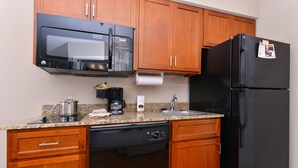 Una cocina compacta con armarios de madera, un microondas negro, un refrigerador negro, un lavavajillas y una encimera de granito.