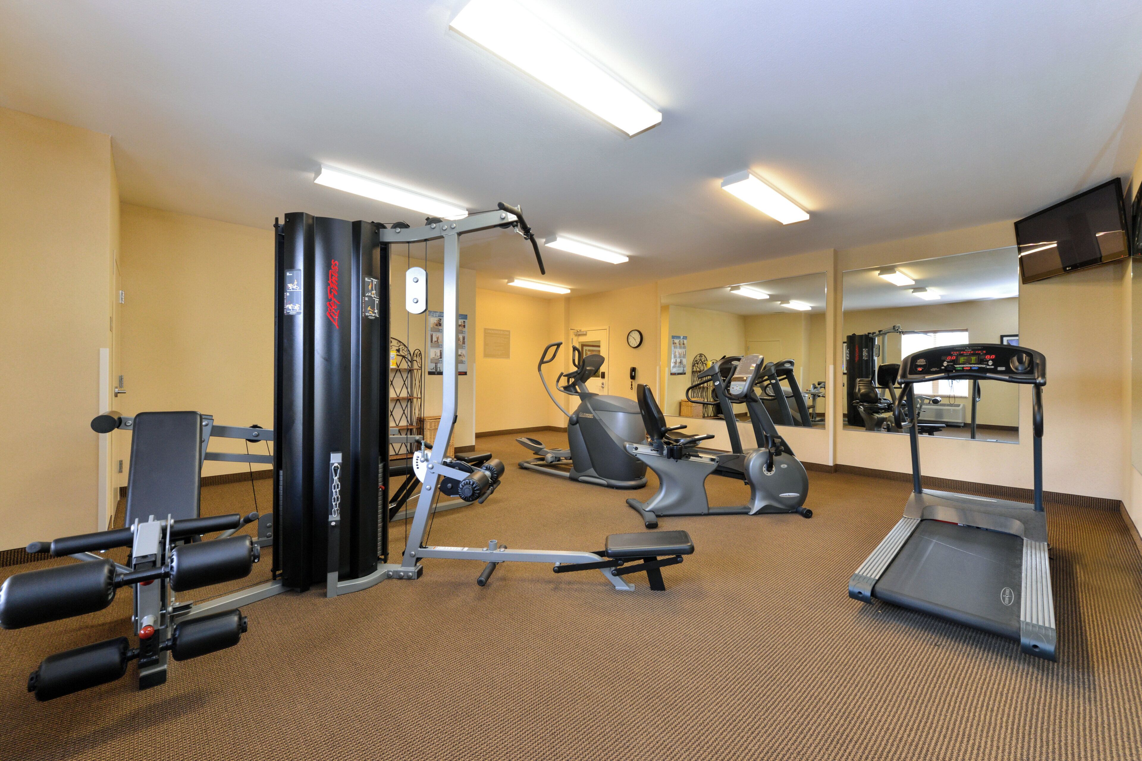 Une salle de sport équipée de divers appareils d’exercice, notamment un tapis de course, un vélo elliptique et des appareils de musculation.