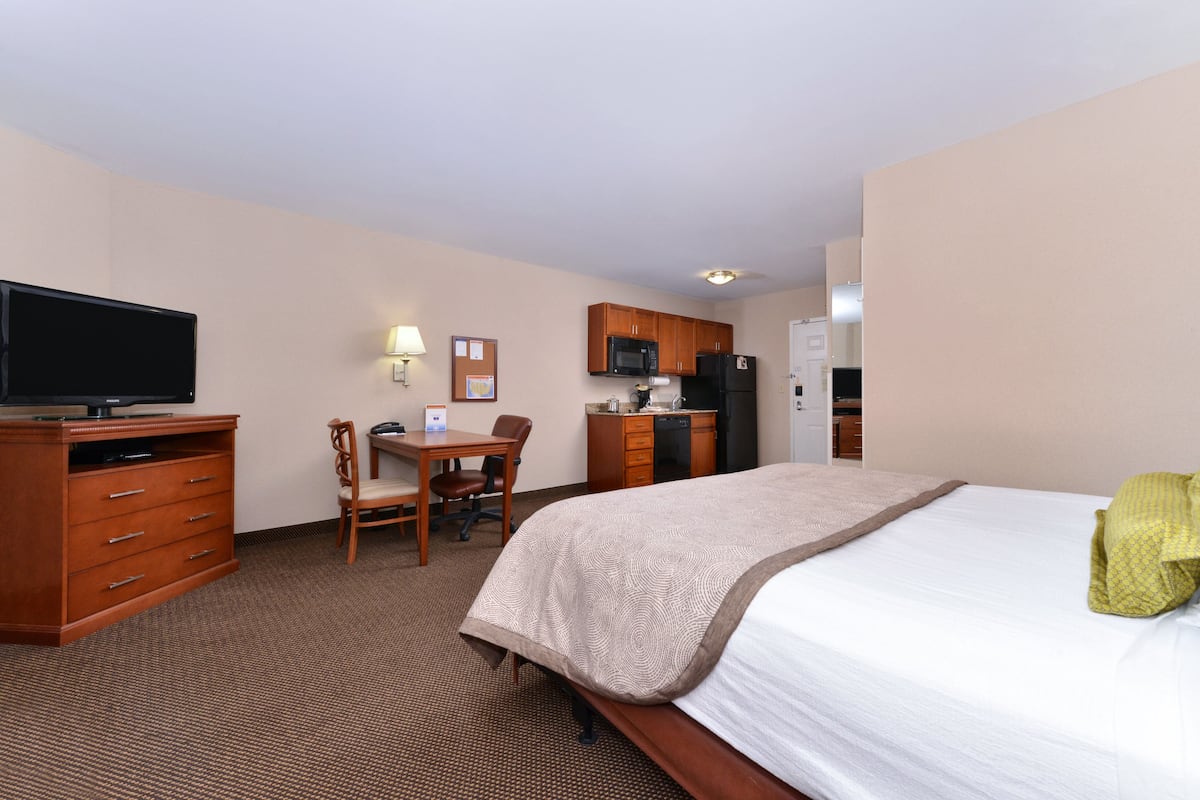 Ein Hotelzimmer mit einem Bett, einem Schreibtisch mit Stuhl, einem Fernseher, einer Mikrowelle und einem Kühlschrank.