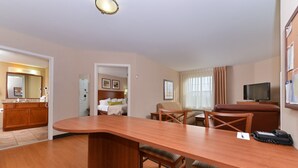 Una habitación de hotel con una mesa de comedor de madera, un televisor, un sofá y una zona de cocina.