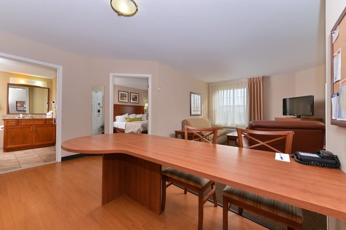 Ein Hotelzimmer mit Holztisch, Fernseher, einer Couch und einer Küchenzeile.
