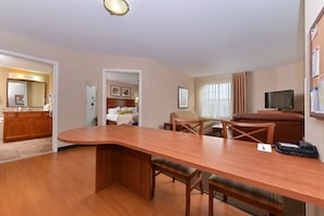 Una habitación de hotel con una mesa de comedor de madera, un televisor, un sofá y una zona de cocina.