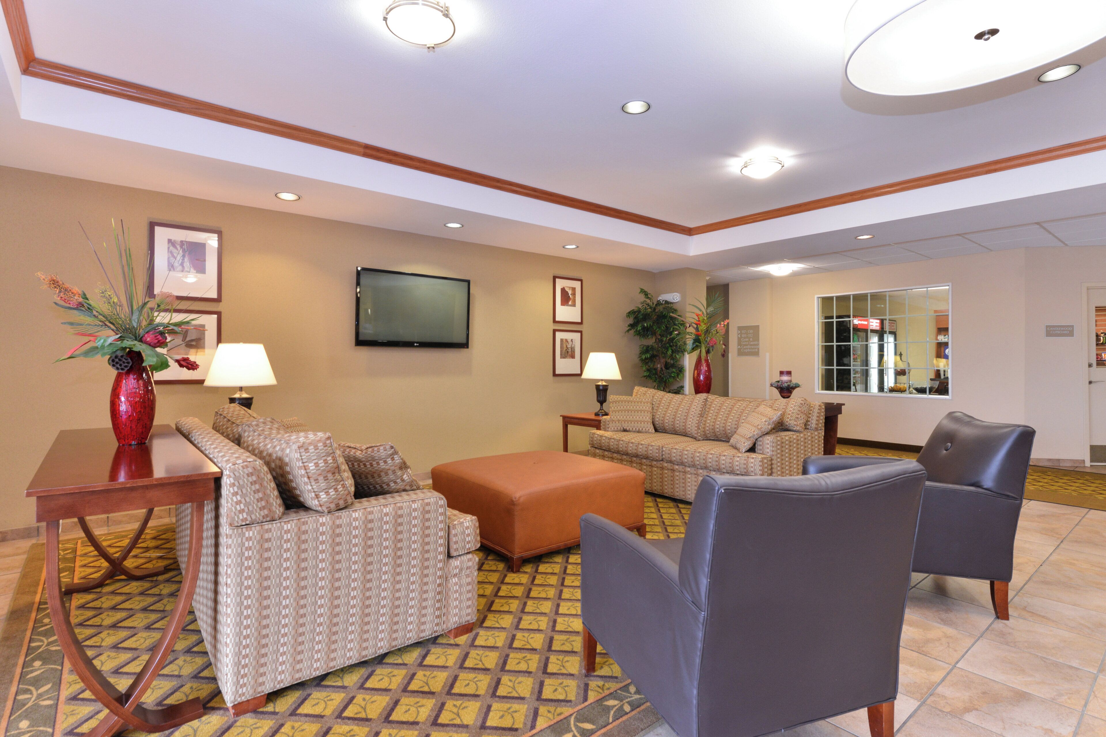A hotel lobby with a checkered floor, sofas, armchairs, a TV, and a reception desk.