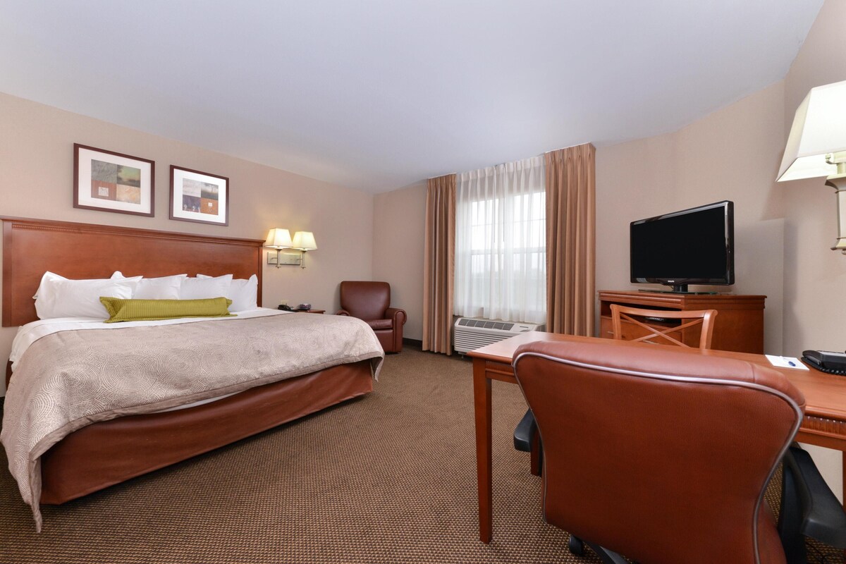 Une chambre d’hôtel avec un grand lit, un bureau, une chaise, une télévision et deux tableaux encadrés au mur.