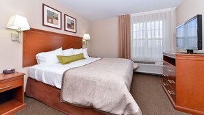 Habitación de hotel con cama, televisión, escritorio y ventana con cortinas.