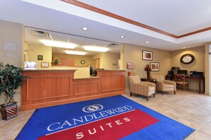 A hotel reception area with a reception desk, two armchairs, a clock, and a blue carpet with 'CANDLEWOOD SUITES' text. - Candlewood Suites Elmira Horseheads by IHG (Horseheads)