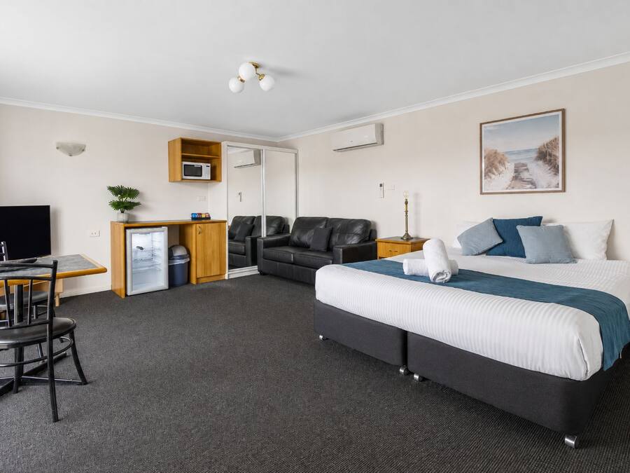 A hotel room with a bed, a desk, a chair, a television, a microwave, and a small refrigerator.