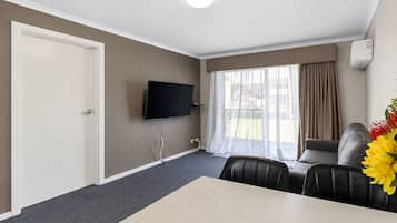 Une chambre d’hôtel équipée d’un téléviseur à écran plat fixé au mur, d’une table à manger avec des chaises, d’un canapé et d’une fenêtre avec des rideaux.