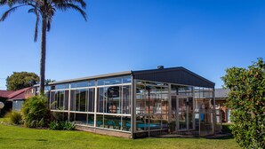 A modern glass building with a pool, surrounded by greenery and a clear blue sky. - Arkana Motor Inn & Terrace Apartments (Mount Gambier)