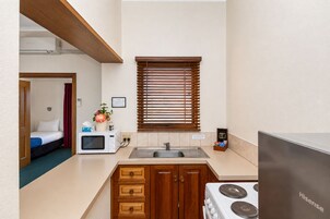 Una kitchenette compacta con microondas, pileta y estufa, placares de madera y una ventana con persianas.