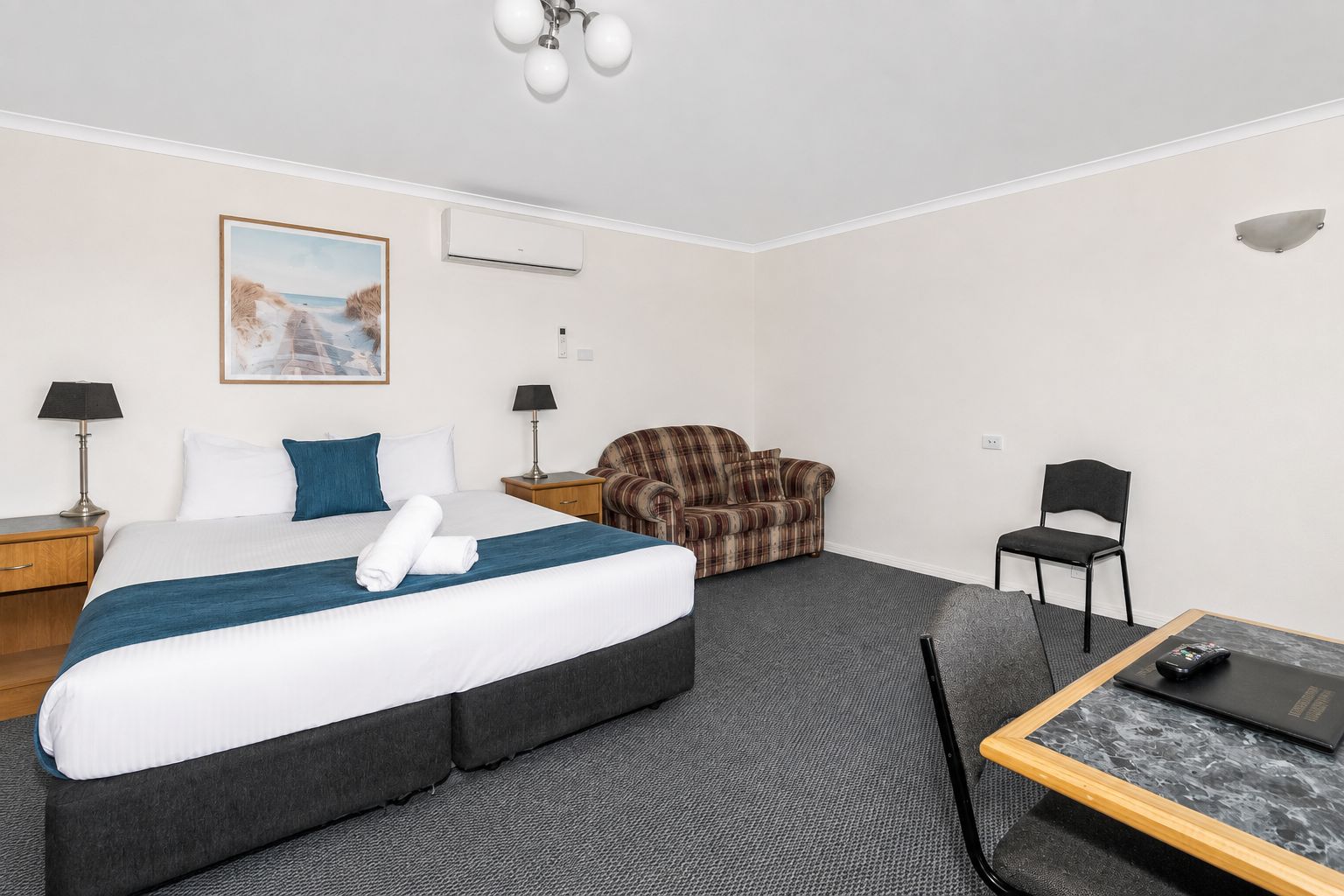 A hotel room with a bed, a sofa, a chair, a desk, and a lamp.