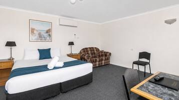 A hotel room with a bed, a sofa, a chair, a desk, and a lamp.