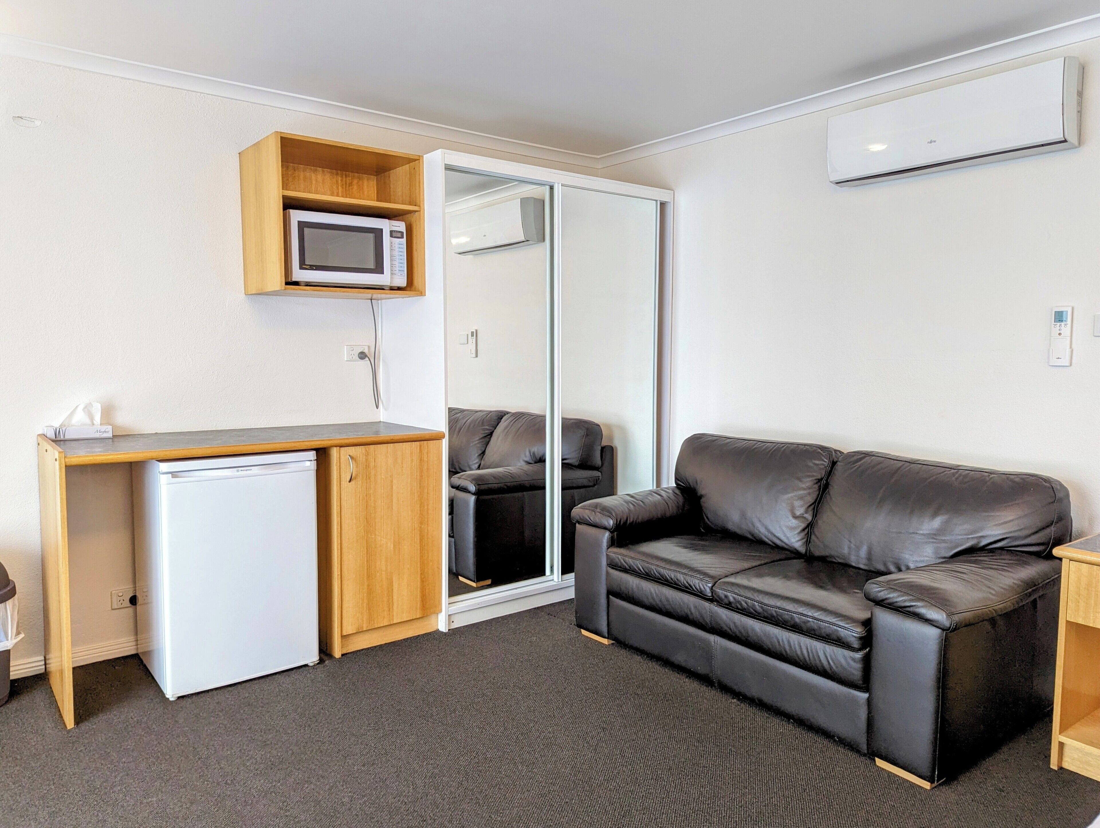 A compact room with a kitchenette, a leather sofa, and a sliding glass door closet.