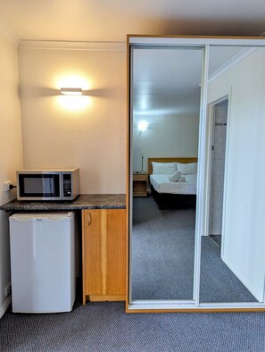 A compact hotel room with a kitchenette, a bed, and a bathroom visible through a sliding door.