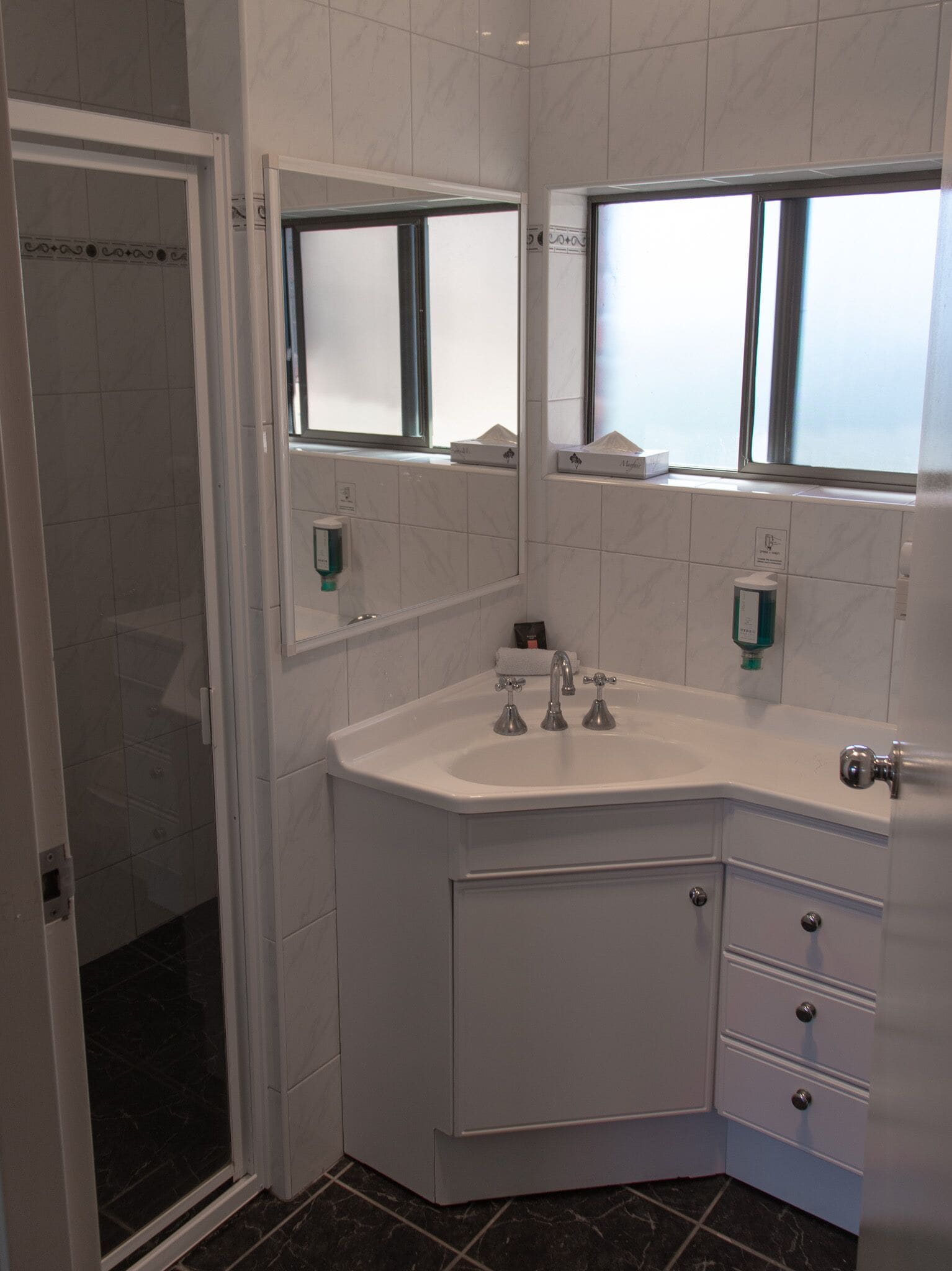 A modern bathroom with a corner sink, two mirrors, a shower, and a toilet.