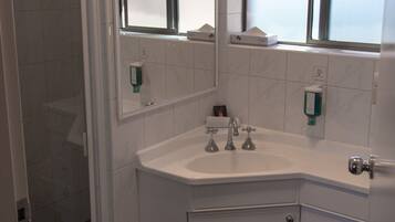 A modern bathroom with a corner sink, two mirrors, a shower, and a toilet.