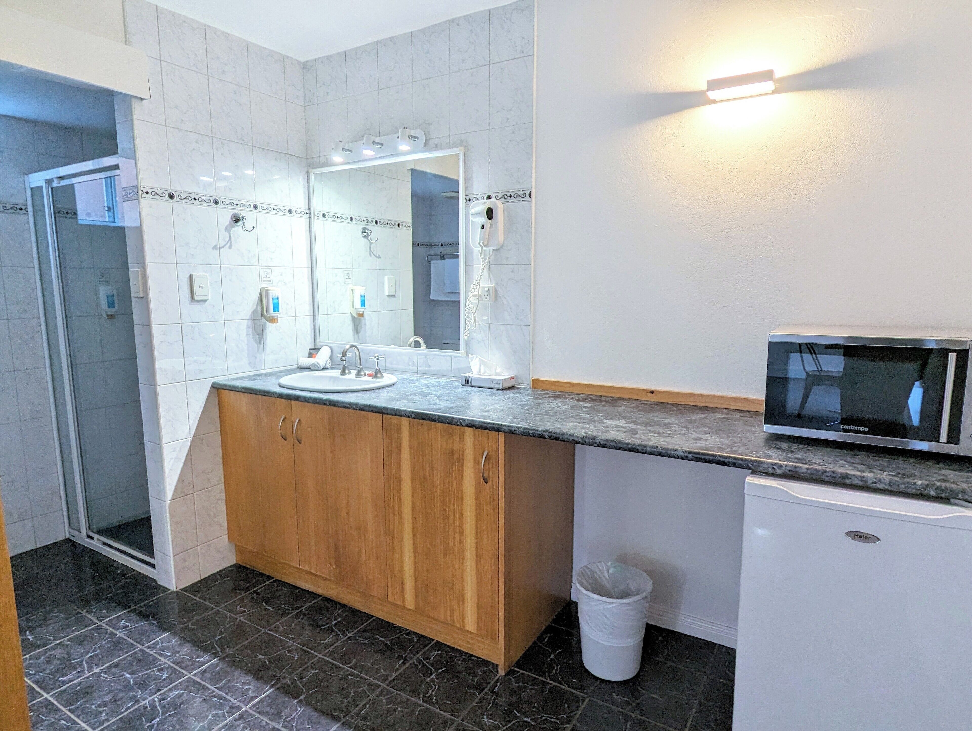 A bathroom with a sink, mirror, vanity, and a microwave.