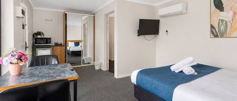 Une chambre d’hôtel avec un lit, un bureau, une chaise, un téléviseur fixé au mur et, au fond, une petite kitchenette.